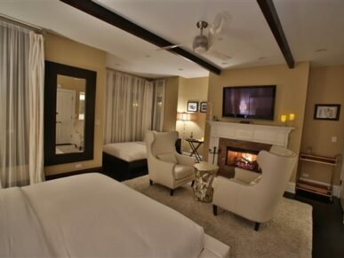 bedroom with white furnishings, blazing fireplace, tv above